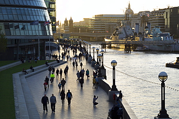 Pedestrians silhouetted on More Place riverfront with City Hall and HMS Belfast behind, London, England, United Kingdom, Europe