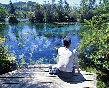 A tourist sitting on the edge of Pupu springs, largest freshwater spring in New Zealand, at Golden Bay, South Island, New Zealand, Pacific