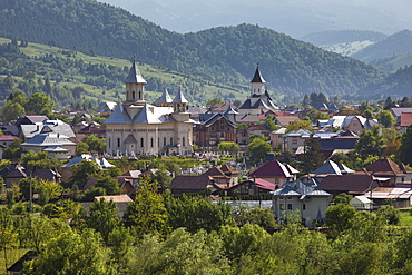 Town nestled in valley in foothills of Carpathian Mountains where churches are the dominant buildings in the village, Varma, Transylvania, Romania, Europe