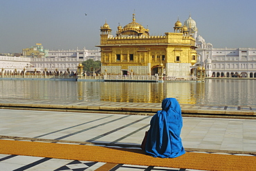A pilgrim in blue sits by the Holy Pool of Nectar at the Golden Temple, centre of the Sikh religion, Amritsar, Punjab, India
