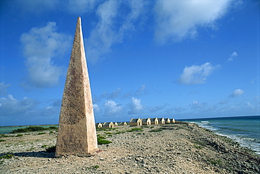 An obelisk on the beach to guide ships in up the salt, with old slave huts behind, near South Point, Bonaire, Antilles, West Indies, Caribbean, Central America