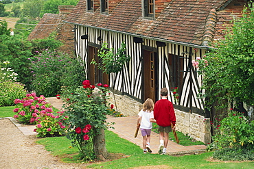 Children carrying baguettes in front of a typical half timbered cottage near St. Pierre sur Dives, in the Calvados region of Basse Normandie, France, Europe