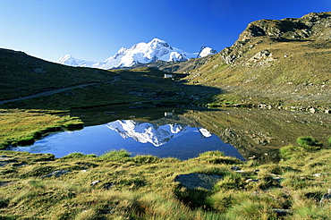 The Breithorn reflected in lake, white chapel in distance on hillside, Zermatt, Valais, Switzerland, Europe