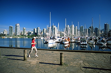 Jogger passing in front of False Creek marina, with downtown skyscrapers behind, Vancouver, British Columbia, Canada, North America