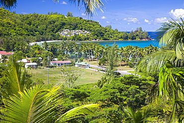 View from hillside across playing field to village and bay, Baie Lazare, Baie Lazare district, Island of Mahe, Seychelles, Indian Ocean, Africa