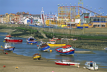 Boats beached on sand banks at low tide in the mouth of the River Clwyd, and the amusement park beyond, Rhyl, north Wales, United Kingdom, Europe