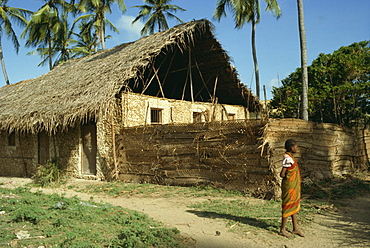 Child stood before traditionally built home, Kenya, East Africa, Africa