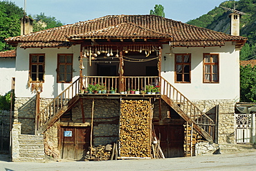 A traditional house with a log store, and gourds and chillies drying in the sun, at Rozhen, Bulgaria, Europe