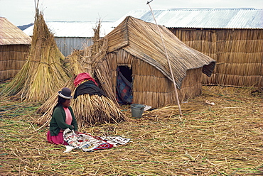 A woman with her sewing sitting outside her reed house in a village at Lake Titicaca, Peru, South America