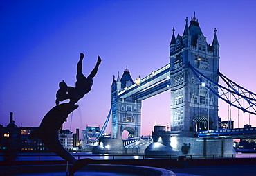 Silhouetted fountain statue and Tower Bridge illuminated at night, London, England, UK