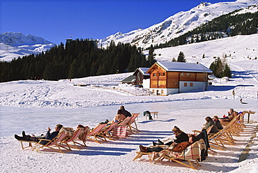 Tourists in deck chairs on the snow in winter at the ski resort of Arosa in the Graubunden region of Switzerland, Europe