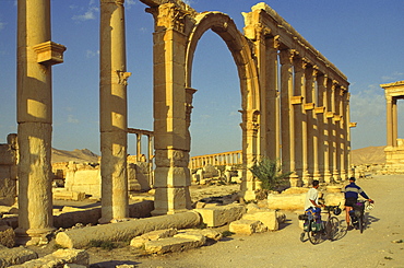 Two cyclists pass the Great Colonnade (Cardo), Palmyra, UNESCO World Heritage Site, Syria, Middle East