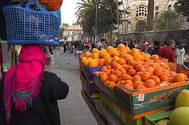 Palestinian woman in colourful scarf and carrying bag on her head walking past an orange stall, Damascus Gate area, Jerusalem, Israel, Middle East