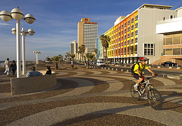 Cyclist on Jerusalem Beach Promenade with Dan hotel facade decorated by Yaaqov Agam in background, Tel Aviv, Israel, Middle East