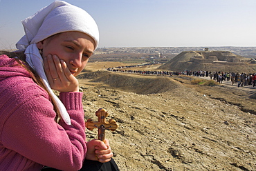 Female pilgrim holding a cross with procession to the Jordan River in background during Christian Orthodox ceremony at Epiphany, Qasr el Yahud, Israel, Middle East