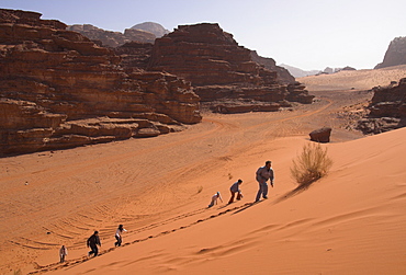 Young people climbing a typical red sand dune with rocks in background, Wadi Rum, Jordan, Middle East