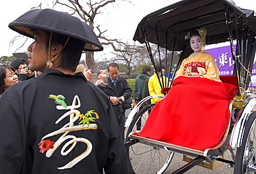 Geisha in full traditional dress and haircut sitting on a rickshaw with red blanket and driver standing in foreground, Higashiyama neighbourhood, Kyoto, Kansai, Honshu, Japan, Asia