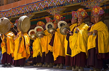 Monks standing in yellow costumes accompanying those dancing with traditional drums, timpani and singing, Hemis Festival, Hemis, Ladakh, India, Asia