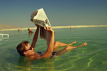 Woman reading a newspaper whilst floating in the Dead Sea, Israel, Middle East