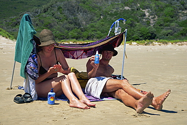 A couple sitting under a beach shade and using skin protection at Wilsons Promontory, Victoria, Australia, Pacific