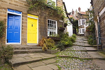 Yellow and blue doors on houses in The Opening, a narrow stepped cobbled alley on steep hill in Old Bay part of the fishing village, Robin Hood's Bay, Yorkshire, England, United Kingdom, Europe