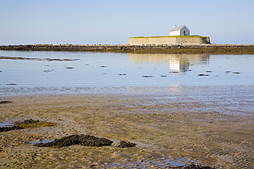 The 12th century Llangwyfan church on small tidal island reflected in calm sea. Porth Cwyfan. Aberffraw. Anglesey, North Wales, United Kingdom, Europe