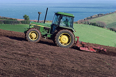 A John Deere tractor with a rotivator on a sloping field in spring, at Holcombe, Devon, England, United Kingdom, Europe