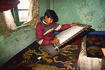 Portrait of a young Tibetan Thangka painter, sitting on a carpet indoors, tangkha paintings used for visualisation in Buddhist meditation, in Darjeeling, India, Asia