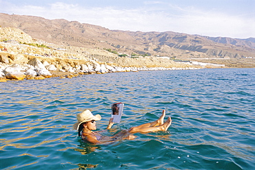 Woman floating in the Dead Sea reading a magazine, Aqaba, Jordan 