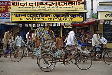 Men riding cycle rickshaws on the street passing the outside of a hotel and restaurant in the city of Dhaka (Dacca), Bangladesh, Asia