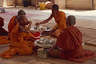 A group of Buddhist monks in saffron robes sitting on the floor, eating, at Wat Chan in Vientiane, Laos, Indochina, Southeast Asia, Asia