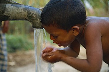 Head and shoulders side view portrait of a young Bangladeshi boy drinking from water pump in a village in Bangladesh, Asia