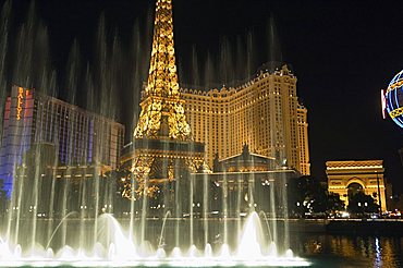 Paris Hotel with mini Eiffel Tower as seen through the fountains of the Bellagio Hotel at night, The Strip (Las Vegas Boulevard), Las Vegas, Nevada, United States of America, North America