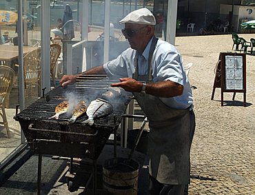 PORTUGAL, ALGARVE, ALVOR, Grilling fresh fish and sardines outside one of many restaurants in the town