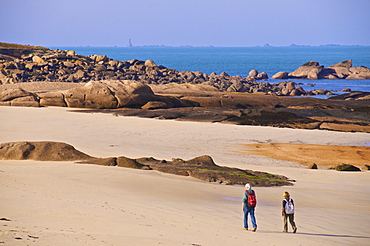 Two people walking along the beach towards the spectacular rocks along the Cote de Granit Rose (Pink Granite Coast) at Ploumanach, Cotes d'Armor, Brittany, France, Europe