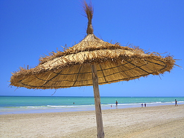 Palm sunshade on the sandy beach, and tourists walking along the sea, Djerba, Tunisia, North Africa, Africa