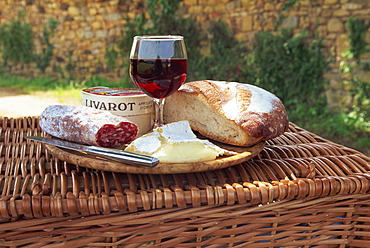 Still life of bread, cheese, glass of red wine and sausage, picnic lunch on top of a wicker basket, in the Dordogne, France, Europe