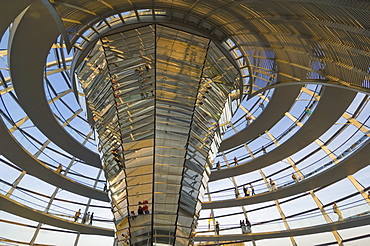 Visitors walk up a spiral ramp around the cone shaped funnel in the dome cupola, which has 360 glass mirrors reflecting light into the Plenary chamber of the Reichstag building, designed by Sir Norman Foster, Berlin, Germany, Europe