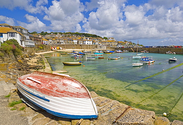 Small unturned boat on the quay and small boats in the enclosed harbour at Mousehole, Cornwall, England, United Kingdom, Europe