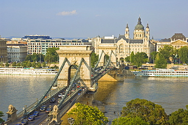 Traffic driving over the River Danube, on The Chain Bridge (Szechenyi Lanchid), with the Gresham Hotel and St. Stephen's Basilica dome behind, Budapest, Hungary, Europe