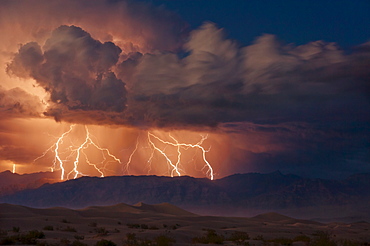 Electrical storm with forked lightning over the Grapevine mountains of the Amargosa Range, Mesquite Flats Sand dunes in the valley, Stovepipe Wells, Death Valley National Park, California, United States of America, North America