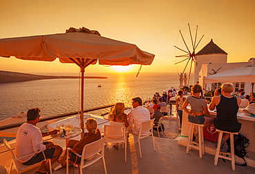 Crowded bar and windmill at sunset by the Aegean Sea, Oia, Santorini (Thira) Cyclades Islands, Greek Islands, Greece, Europe