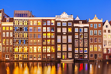 Dutch gables on row of typical Amsterdam houses at night with reflections in the Damrak canal, Amsterdam, North Holland, Netherlands, Europe