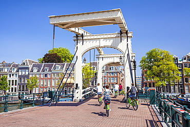 Cyclists riding across the Magere brug (Skinny Bridge) spanning the River Amstel, Amsterdam, North Holland, Netherlands, Europe