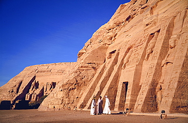 Three traditionally dressed men outside the Temple of Hathor, built in honour of Queen Nefertari, and in the background the colossi of Ramses II, outside the Temple of Re-Herakhte, built for Ramses II, (also known as the Sun or Great Temple of Ramses II), Abu Simbel, (moved to current site when the Aswan High Dam was built), Nubia, Egypt, Africa