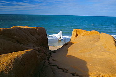 Red rock formations and jangada boat on the seafront of Canoa Quebrada, Canoa Quedrada, Ceara', Brazil, South America