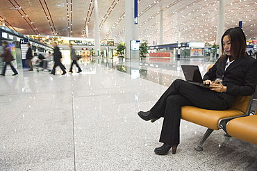 A Chinese business woman using a laptop computer at Beijing Capital Airport part of new Terminal 3 building opened February 2008, second largest building in the world, Beijing China, Asia