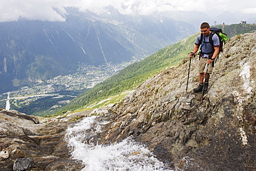 Hiker crossing a stream above Chamonix Valley, Rhone Alps, France, Europe