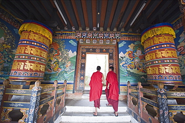 Monks walking between prayer wheels at Trongsa Dzong (Chokhor Raptentse) dating from 1648, Bhutan Asia