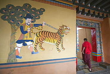 A monk walks past a tiger painting at Paro Rinpung Dzong dating from 1644, Paro, Bhutan, Asia